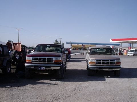 1996 Ford Bronco - Two 1996 Ford Broncos are parked at a gas station under a clear blue sky.