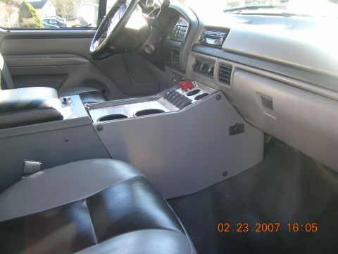 1996 Ford Bronco - The interior of a truck features a custom console with multiple switches and cup holders.