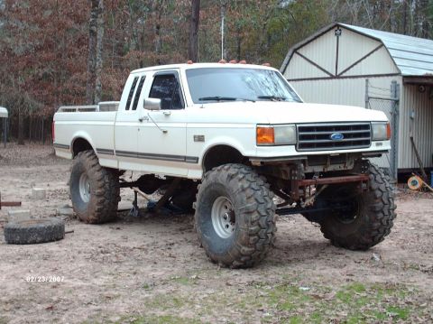 1990 Ford F-150 - This modified Ford pickup truck features oversized tires and a lifted suspension, suggesting off-road capabilities.