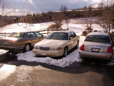 1996 Mercury Grand Marquis - Three sedans, including a 1996 Mercury Grand Marquis, sit parked in the snow during winter.
