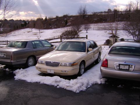 1996 Mercury Grand Marquis - Three sedans are parked in a driveway with snow on the ground and a cloudy sky overhead.