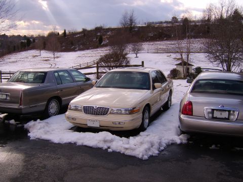 1996 Mercury Grand Marquis - Three sedans are parked in a snowy driveway on a cloudy day.