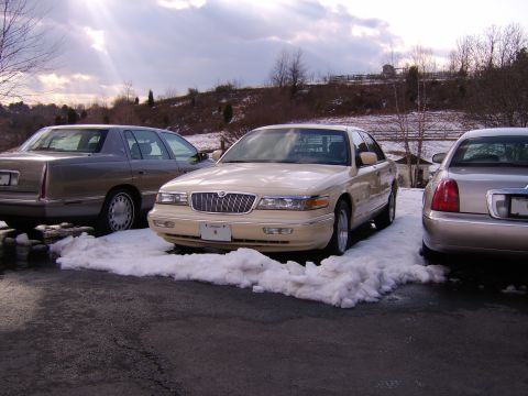 1996 Mercury Grand Marquis - A cream 1996 Mercury Grand Marquis is parked in the snow, with two other sedans visible.