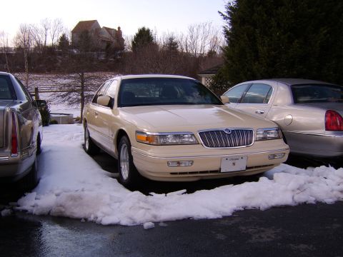 1996 Mercury Grand Marquis - Two sedans are parked in a snowy driveway during the day.