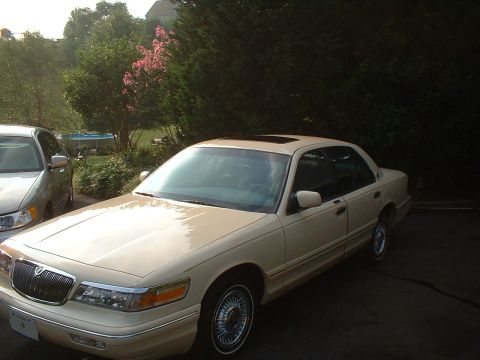 1996 Mercury Grand Marquis - A tan 1996 Mercury Grand Marquis sedan is parked next to another car in a driveway.
