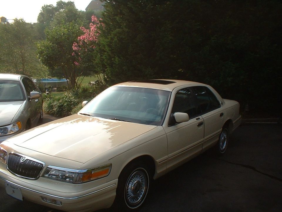 Cream Mercury Grand Marquis sedan parked on driveway, front 3/4 view