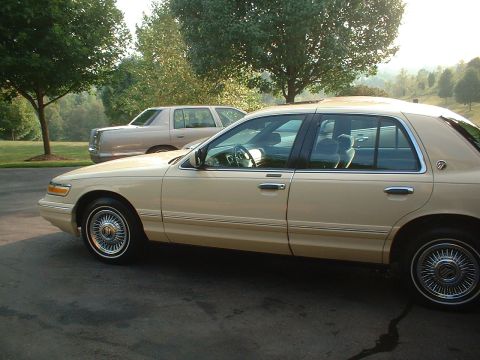 1996 Mercury Grand Marquis - Side view of a tan 1996 Mercury Grand Marquis parked outdoors with another vehicle in the background.