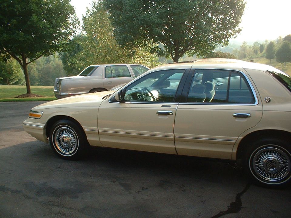 Tan Mercury Grand Marquis sedan, side view, with chrome wire wheels, parked on driveway.
