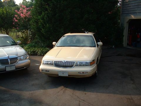 1996 Mercury Grand Marquis - Two sedans, one a 1996 Mercury Grand Marquis, are parked in a driveway with trees and a garage visible.
