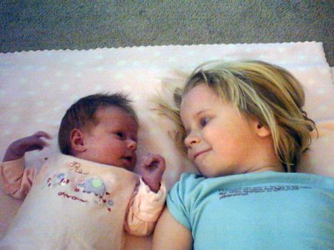 2002 Oldsmobile Aurora - A baby and a young child share a tender moment while lying on a blanket.