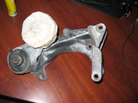 1991 Ford Bronco - Engine mount bracket with a rubber bushing and a covered component, resting on a wooden surface.
