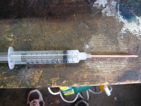 1968 Shelby GT500 - A close-up view of a syringe with a copper tube, resting on a weathered wooden surface.