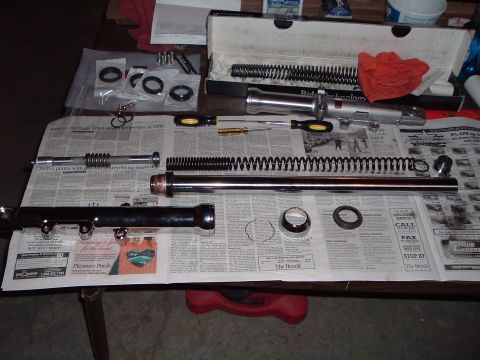 2000 Harley-Davidson Sportster - Motorcycle front fork components, including springs and sliders, are disassembled and arranged on a table covered with newspapers.