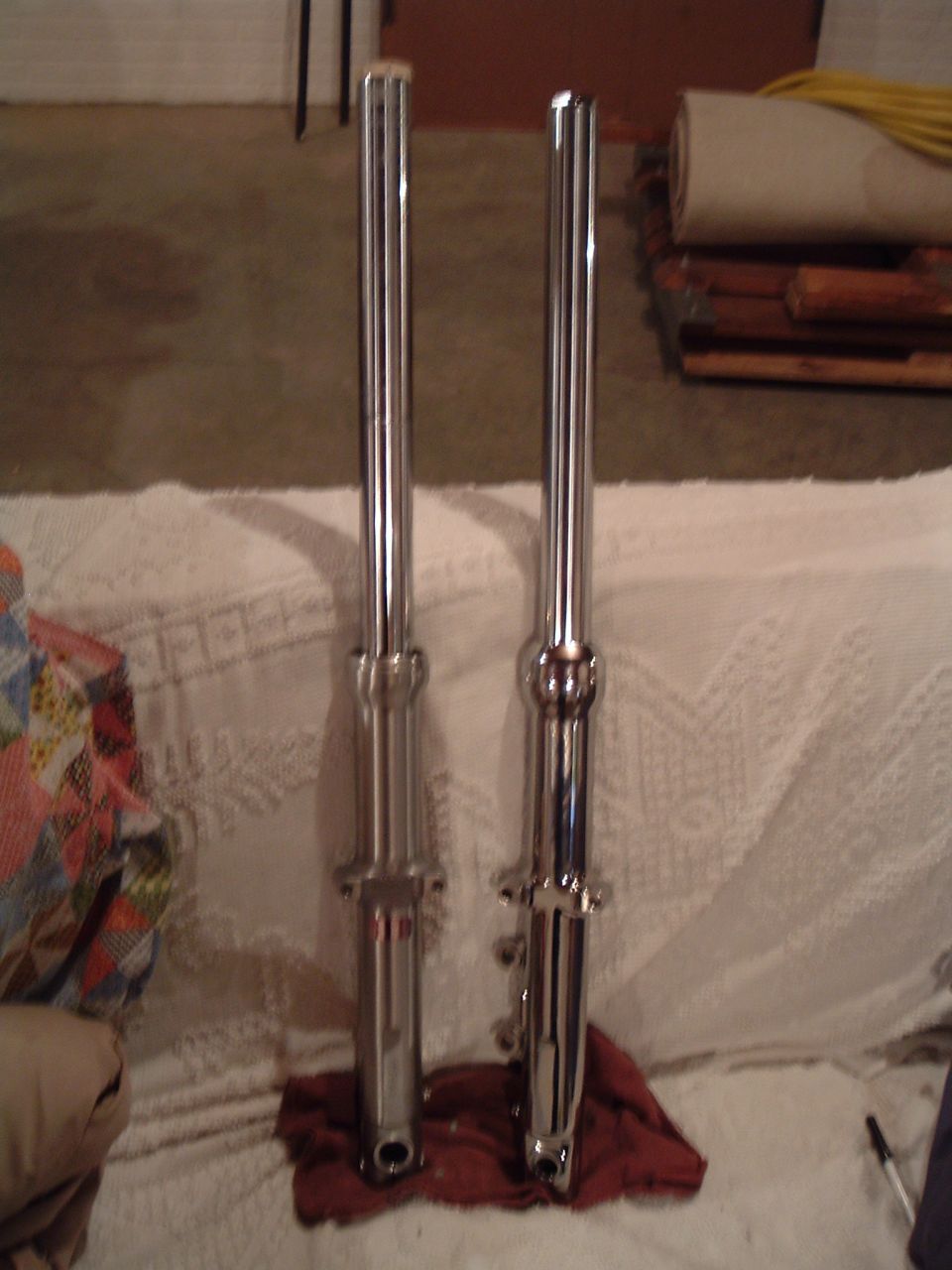 Pair of chrome motorcycle front fork legs standing upright on a blanket in a garage