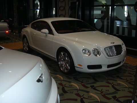 1996 Ford Crown Victoria - A white Bentley Continental GT is displayed at an auto show, with another white vehicle partially visible in the foreground.