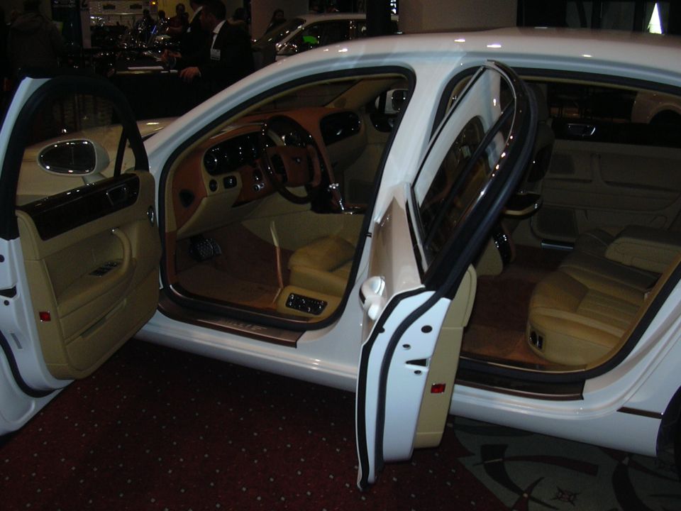 Interior view of a white luxury sedan with tan leather seats and wood trim, doors open