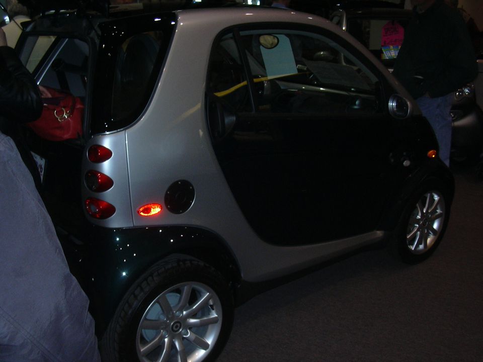 Smart Fortwo with black doors and silver roof, rear quarter view. Red bag visible in open trunk
