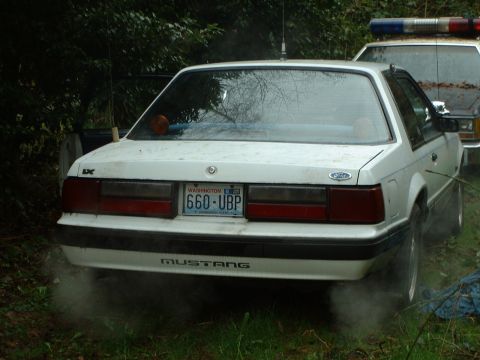 1987 Ford Mustang - A white 1987 Ford Mustang is parked next to a police vehicle.