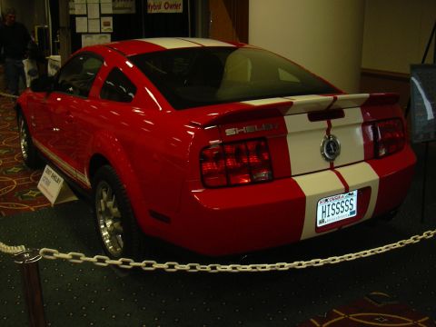 1996 Ford Crown Victoria - A red 2007 Shelby GT500 with white racing stripes is displayed at an auto show.