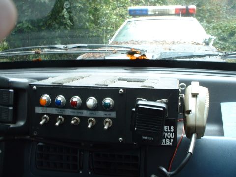1987 Ford Mustang - Custom switch panel and radio installed in a police car interior, with a light bar visible outside.