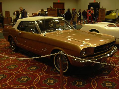 1996 Ford Crown Victoria - A classic gold convertible is displayed indoors with other vehicles and people in the background.