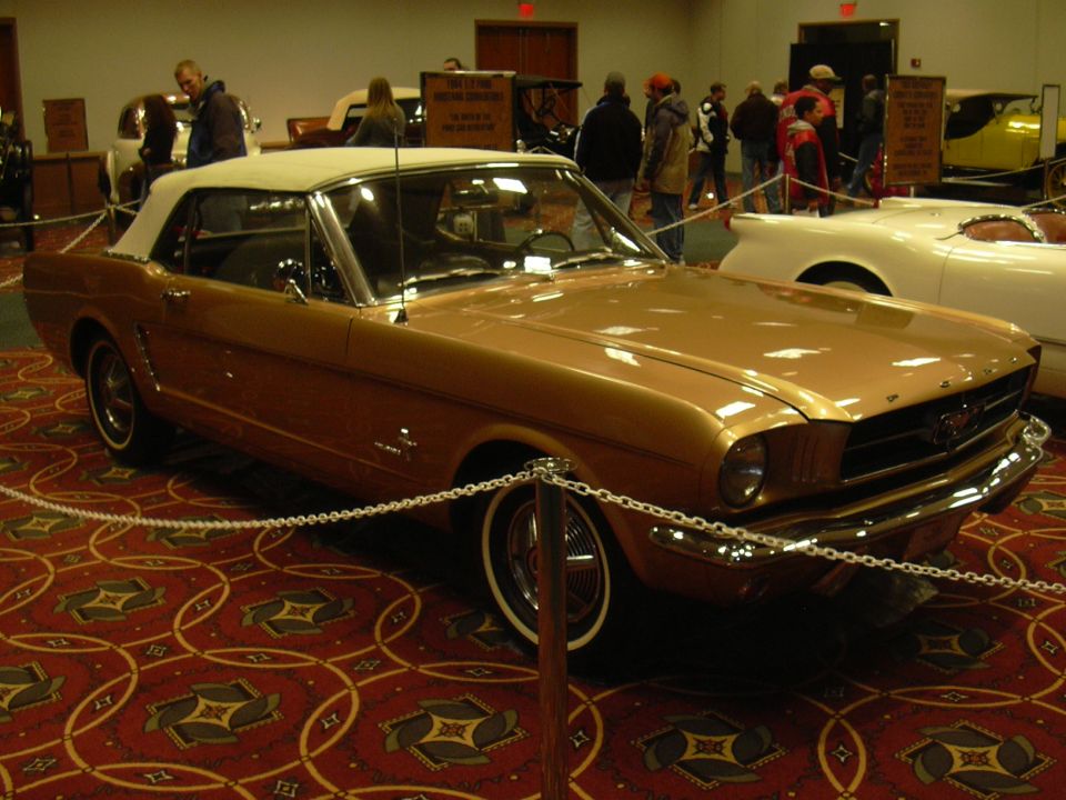 Gold convertible with white top, front end visible. Another white car is next to it