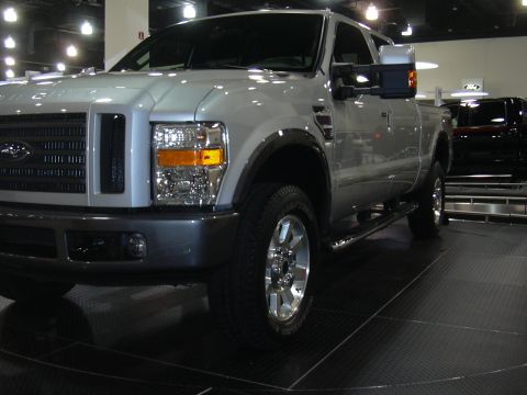 1996 Ford Crown Victoria - A silver pickup truck is displayed at an auto show, with another dark vehicle visible in the background.