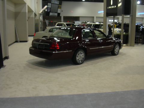 1996 Ford Crown Victoria - A maroon Mercury Grand Marquis is displayed indoors, possibly at an auto show, with other vehicles visible.
