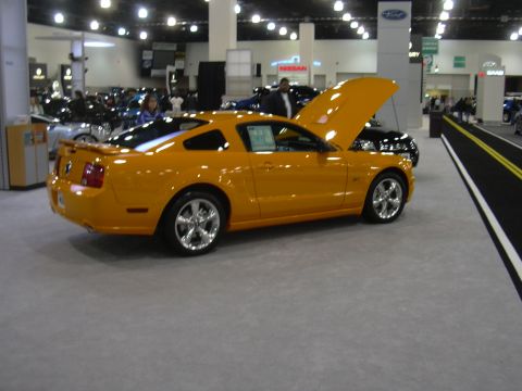 1996 Ford Crown Victoria - Yellow Ford Mustang coupe on display at an auto show with the hood open.