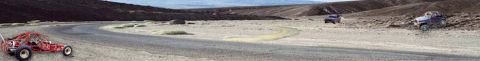 1989 Ford Bronco - Wide panoramic desert scene with a red tube-frame sand rail or buggy parked at left, a dark SUV in the middle distance and a blue lifted 4x…