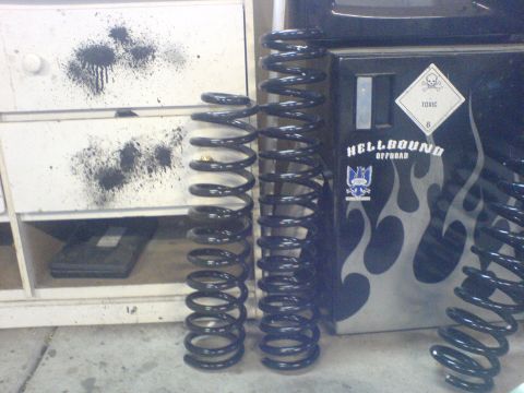 1967 Ford Bronco - Coil springs are displayed in front of a cabinet with 'Hellbound Offroad' branding and flame decals.