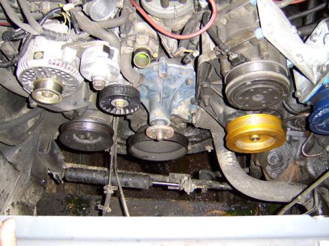 1989 Ford Bronco - Front engine accessory drive area viewed from above, showing the alternator with ribbed pulley at upper left, a black serpentine belt tensi…