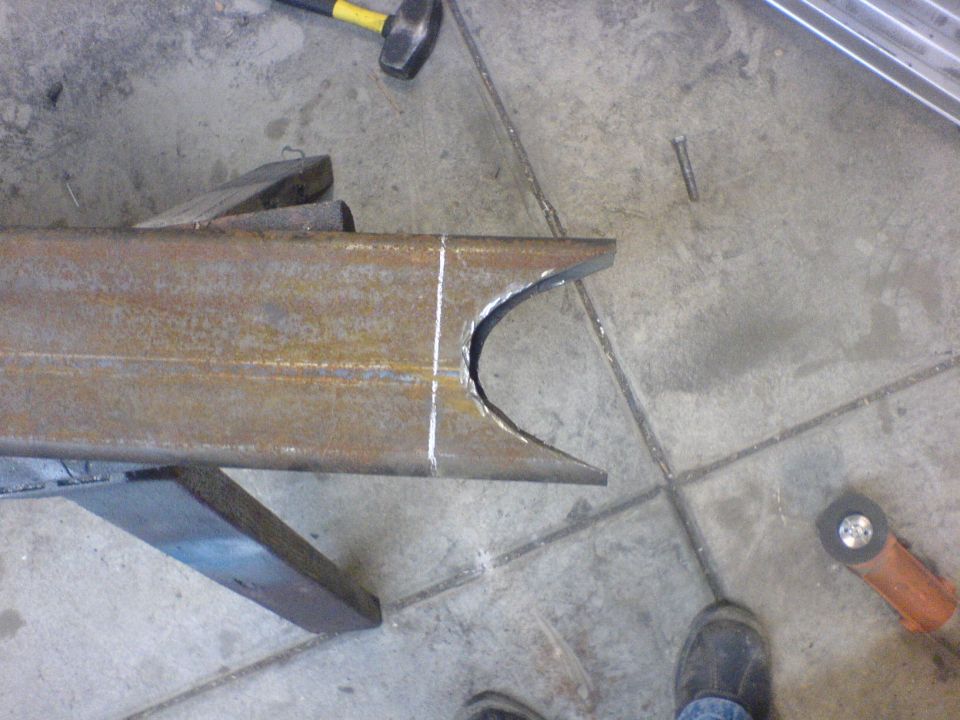 Rusty metal frame section with a curved cut, resting on a wooden block. A hammer and grinder are nearby