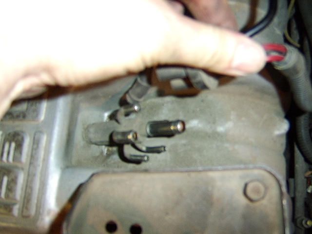 Hand pointing to engine bay vacuum or wiring connectors on a dusty component