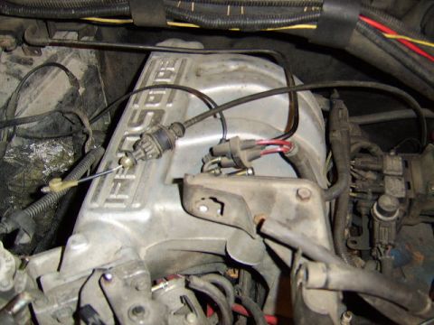 1989 Ford Bronco - Close-up of an aluminum valve cover with raised 'FORD' lettering on an inline engine, showing routed vacuum lines, wiring connectors with r…