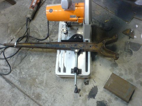 1967 Ford Bronco - A suspension arm is prepared for cutting on a chop saw in a workshop.