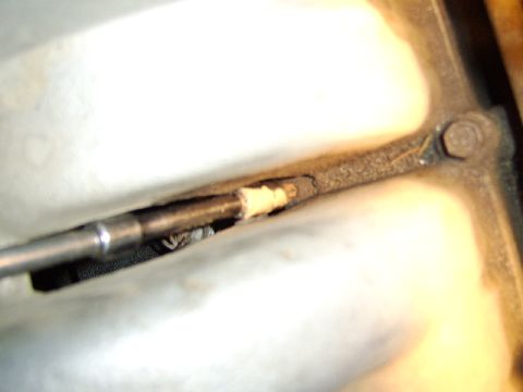 1989 Ford Bronco - Extreme close-up of a metal engine component with a dark bracket or arm bolted in place, showing signs of grime and wear next to polished m…