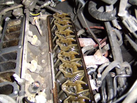 1989 Ford Bronco - Close-up of an exposed engine cylinder head with the valve cover removed, showing a row of oil-coated rocker arms, valve springs, and pushr…