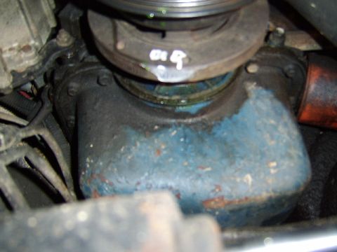 1989 Ford Bronco - Close-up engine bay view of a weathered engine component, showing a blue-painted cast part with surface rust and a round pulley/damper abov…