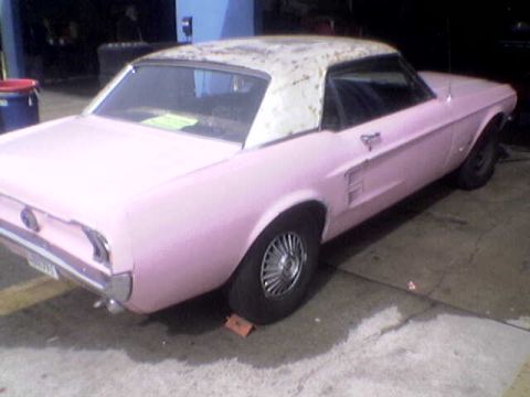 1988 Ford Bronco - A pink classic coupe with a white hardtop sits parked on a concrete surface.