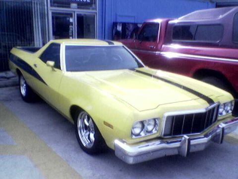 1988 Ford Bronco - A yellow coupe utility with racing stripes is parked next to a red pickup truck.
