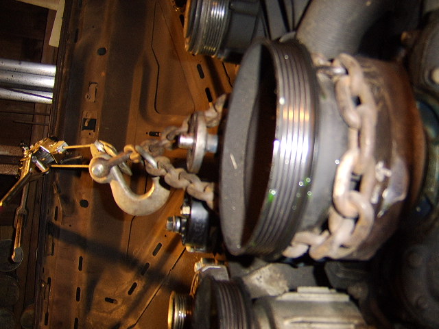 Engine crankshaft pulley with a chain and hook wrapped around it for lifting.