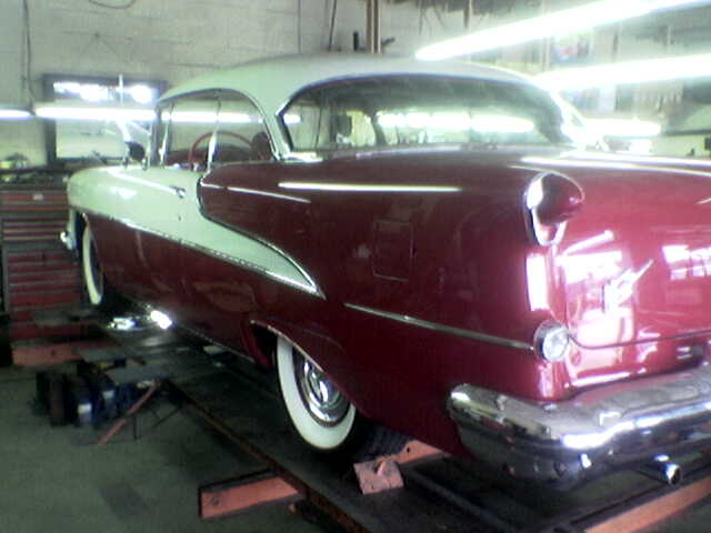 Two-tone red and white classic car on a lift, rear quarter view. Chrome bumper, whitewall tires