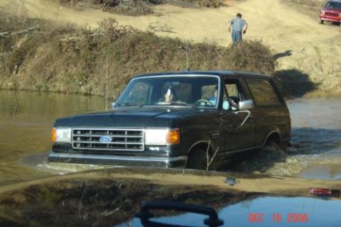 1990 Ford Bronco - A black Ford Bronco navigates a muddy water obstacle, with another vehicle visible in the background.
