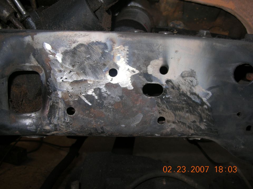 Bare-metal truck frame crossmember with grinder marks and drilled mounting holes