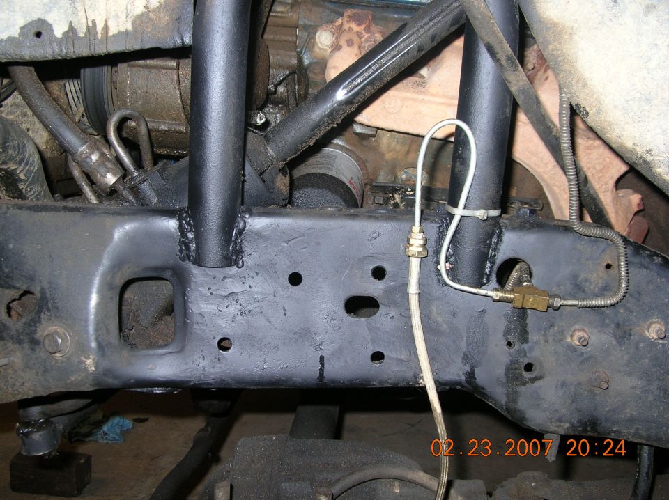Black tube legs welded to truck frame rail with brake line tee, viewed from below