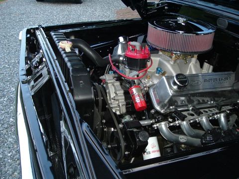1966 Ford F-100 - The engine bay of a black vehicle showcases a powerful Ford V8 engine with performance upgrades.