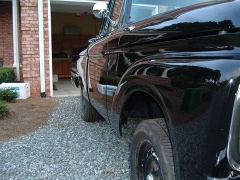 1966 Ford F-100 - This black 1966 Ford F-100 pickup truck is seen from the side, parked near a garage entrance.