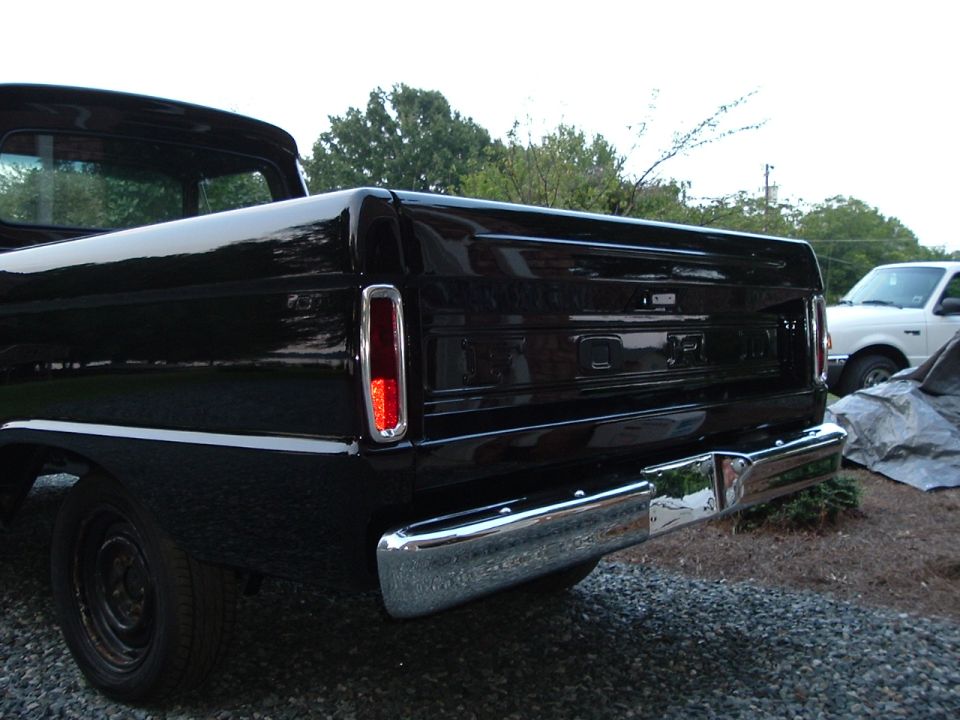Rear of black Ford pickup with FORD tailgate lettering and chrome bumper on gravel lot