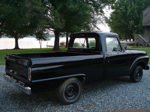 1966 Ford F-100 - This black 1966 Ford F-100 pickup truck is parked on a gravel driveway near a body of water.